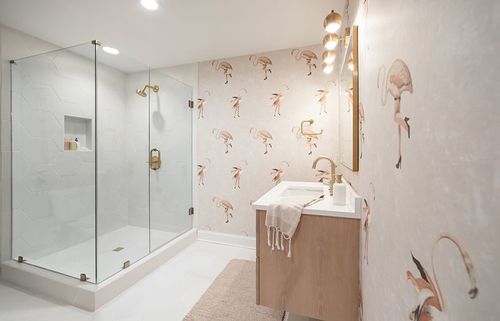 Quirky flamingos sit atop a watercolor blush background and clean white fixtures. Brass accents bring an added warmth to the space.