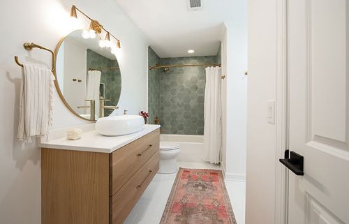 Sage green tile in a honeycomb pattern makes this shower a standout. Warm brass cabinet hardware and light fixtures compliment the medium-stain wood floating vanity.