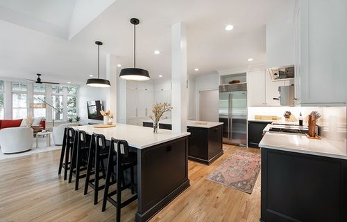 High contrast design scheme with bright white countertops and coal black painted lower cabinets. Double islands face each other underneath modern black pendant lights.